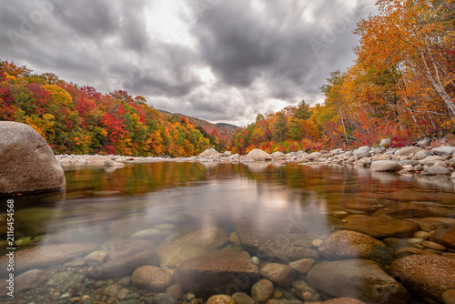Autumn river landscape with vibrant fall foliage and cloudy sky reflection
