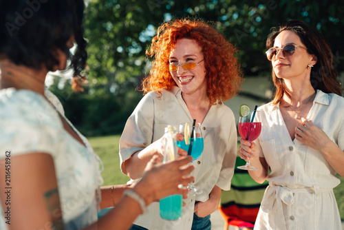 Sticker Diverse young women gathering outdoors, laughing and drinking cocktails at a sum