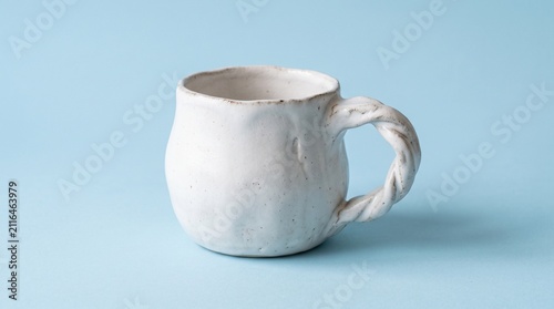 Minimalist handmade ceramic white mug with a unique twisted handle, isolated on a clean light blue background.