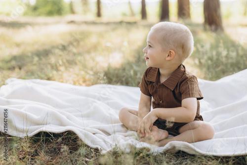 Fotografie Young boy sitting on a white blanket outdoors in a sunny park, enjoying innocenc