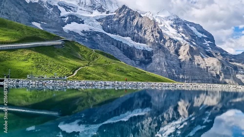 pristine Fallboden lake in the Swiss Alps with reflection of snowy Eiger Monch peaks in turquoise water, passing train, peaceful Switzerland landscape in idyllic summer morning 