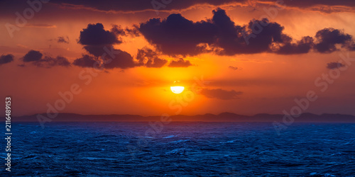 Dramatic ocean sunset with vibrant orange sky and dark clouds over the horizon