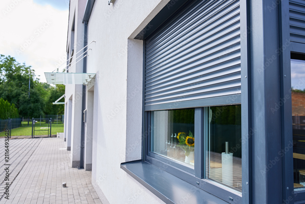 Fototapeta premium Roller shutter partly covers window on the exterior of modern house