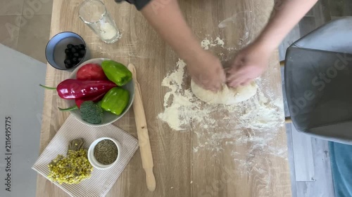 The hands of a female cook knead a lump of dough on a wooden table with white wheat flour.