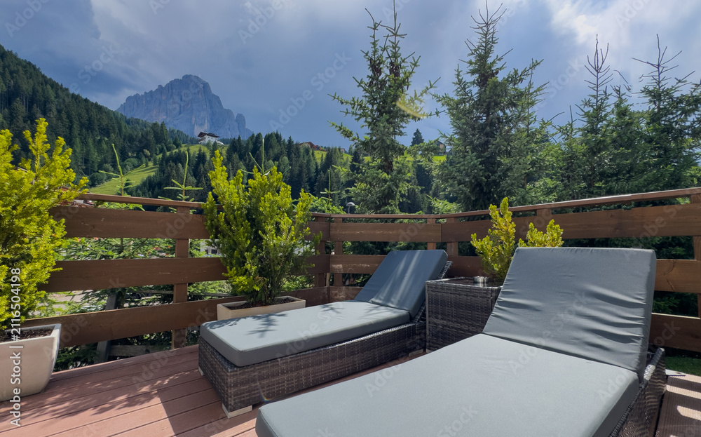 Obraz premium Awesome photo of cozy wooden balcony with comfortable lounge chair overlooking scenic green mountains. 
