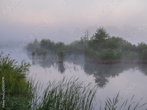 Foto A serene, misty morning landscape features a calm river reflecting lush green tr