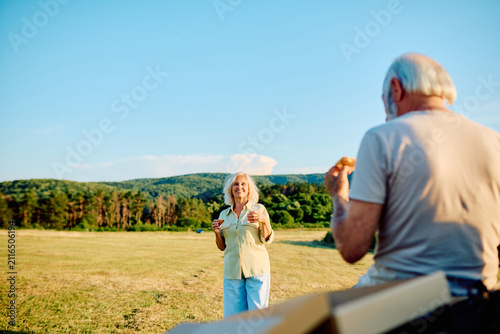 Obraz na płótnie Senior couple sharing a happy moment, eating picnic snacks outdoors in a field,