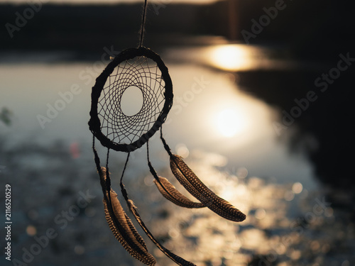 The willow dreamcatcher evolves in the wind by the water at sunset
