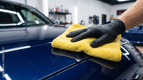 Meticulous final wipe down of reflective dark blue car paint with yellow microfiber towel