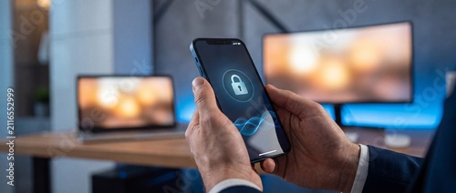 Close up of a person holding a smartphone with a lock icon on the screen in a modern office setting with contemporary office environment environment computer monitors