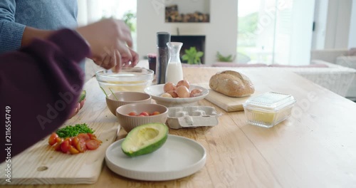Meal prep starting on wooden countertop with hands halving avocado and whisking eggs for breakfast