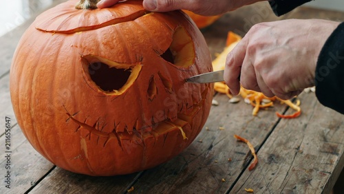 A close up view of a person carving a spooky face into a fresh orange pumpkin for the halloween holiday