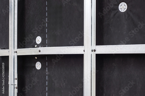A wall under construction with metal studs and a black membrane, prepared for insulation.