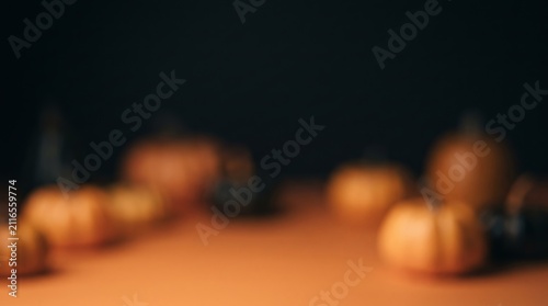 A blurred arrangement of small orange pumpkins and autumn leaves rests on a dark surface against a glowing gradient background.