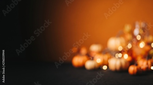 A blurred arrangement of small orange pumpkins and autumn leaves rests on a dark surface against a glowing gradient background.
