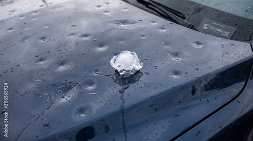 A piece of hail rests on a car hood damaged by severe weather.
