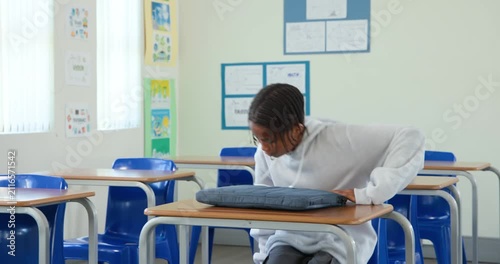 Teen African male in gray hoodie finding empty school desk placing backpack opening laptop to study