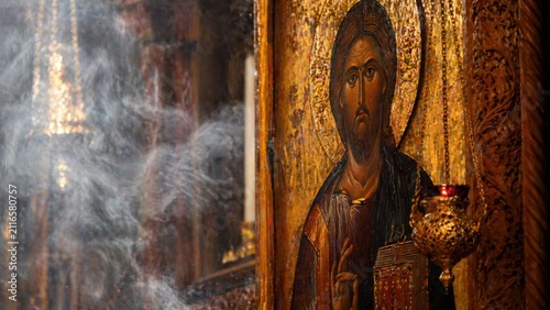 Religious icon of Jesus Christ displayed in an ornate frame, surrounded by incense smoke and candlelight in a traditional church interior