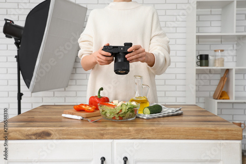 Female photographer with camera taking picture of vegetable salad on table in...