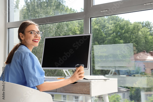 Young female medical student in eyeglasses studying with modern computer at w...