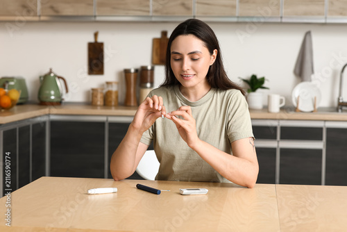 Diabetic young woman using glucose test strip in kitchen