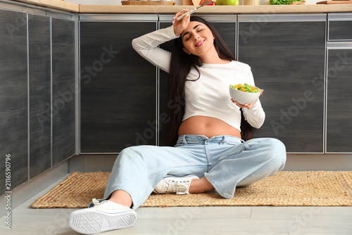 Beautiful young pregnant woman with bowl of fresh vegetable salad sitting on ...