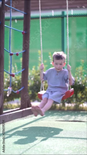 Cheerful little boy enjoying swing ride at outdoor park on a beautiful sunny day.