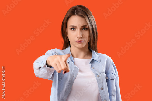 Young woman pointing at viewer on orange background, closeup. Accusation concept