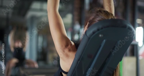 Back view of a fit young woman doing incline dumbbell shoulder press