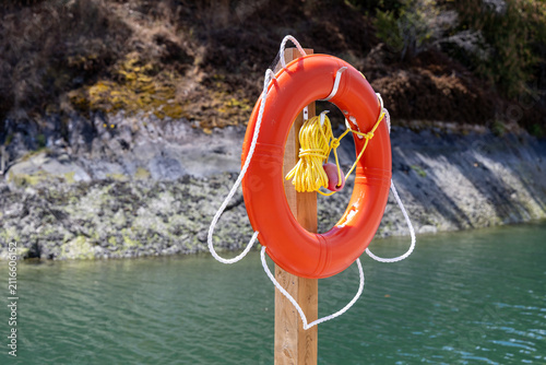 Картината върху платно Orange Lifebuoy Life Ring On Wooden Post With Rope By Calm Water For Safety And