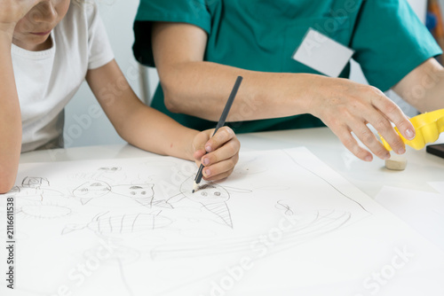 Konstfotografi A left-handed child holds a pencil and draws on paper beside a healthcare profes