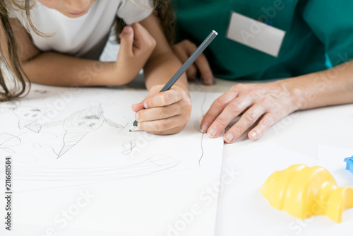 Foto High-angle close-up of colorful pencils on table with a left-handed child drawing on paper accompanied by a therapist