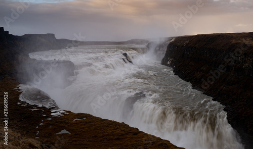 Obraz na płótnie Powerful torrent of the hvita river cascading into a deep canyon, creating mist and spray under a cloudy sky at sunset