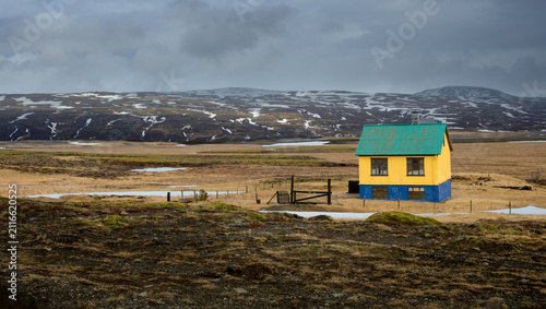 Charming isolated yellow house with a green roof in a desolate Icelandic tundra landscape under dark stormy skies.