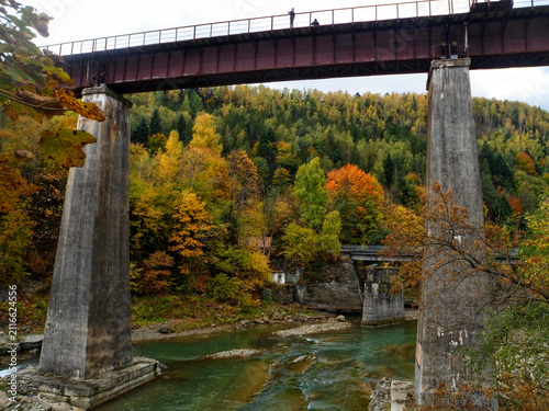 A high railway bridge spanning across a mountain river with colorful autumn trees