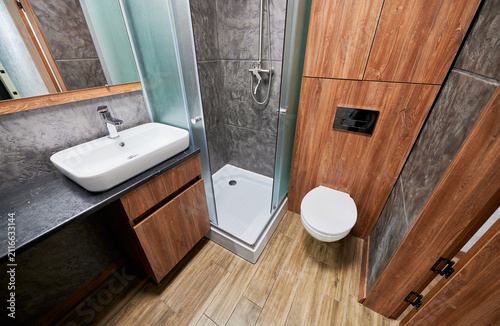 Modern bathroom interior with vessel sink, shower cabin and wall mounted toilet. Stylish loft washroom with wooden panels, dark textured walls and contemporary design