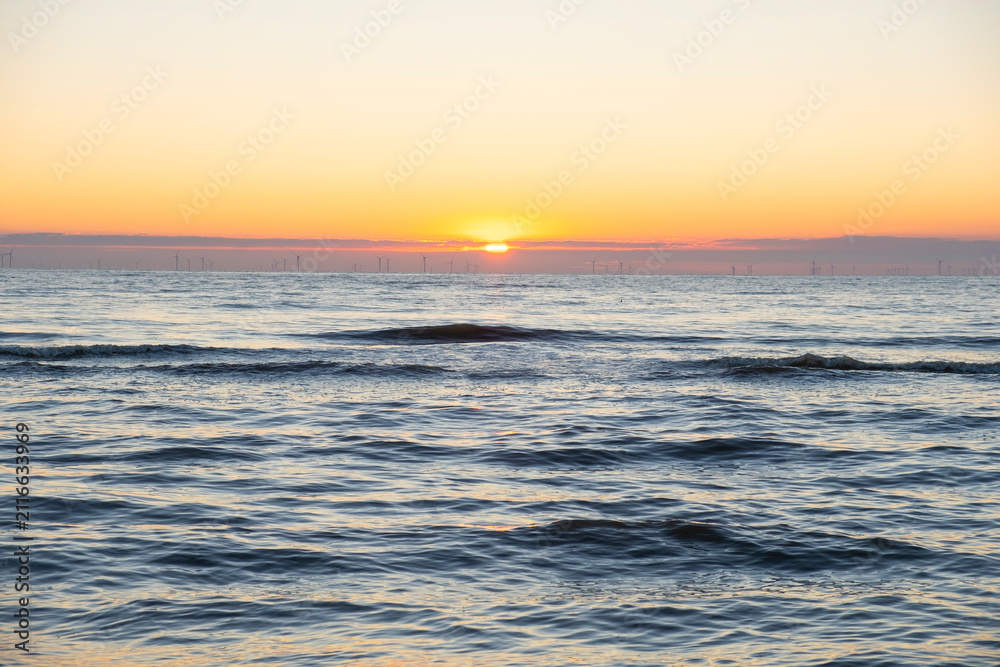 Fototapeta premium Minimalist seascape with a golden sunset over the calm sea and a clear sky.