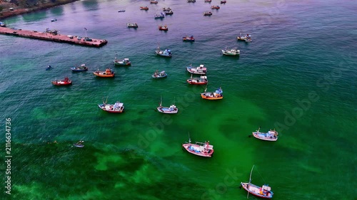 Aerial view of numerous small fishing boats anchored in the clear turquoise waters of a bay with a pier visible in the background in Sri Lanka.