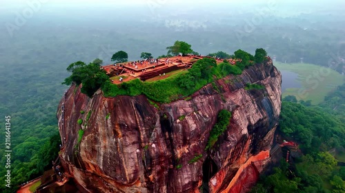 Aerial view of the ancient Sigiriya Rock Fortress rising above the lush green jungle canopy with visitors exploring the historic ruins on the summit in Sri Lanka.