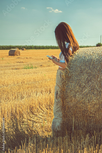 фотографія A vintage portrait of a teenage girl finds a quiet moment in a nostalgic hayfield, absorbed in her smartphone