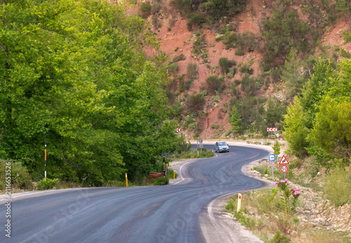 Winding asphalt mountain road with a car driving through a lush green forest landscape