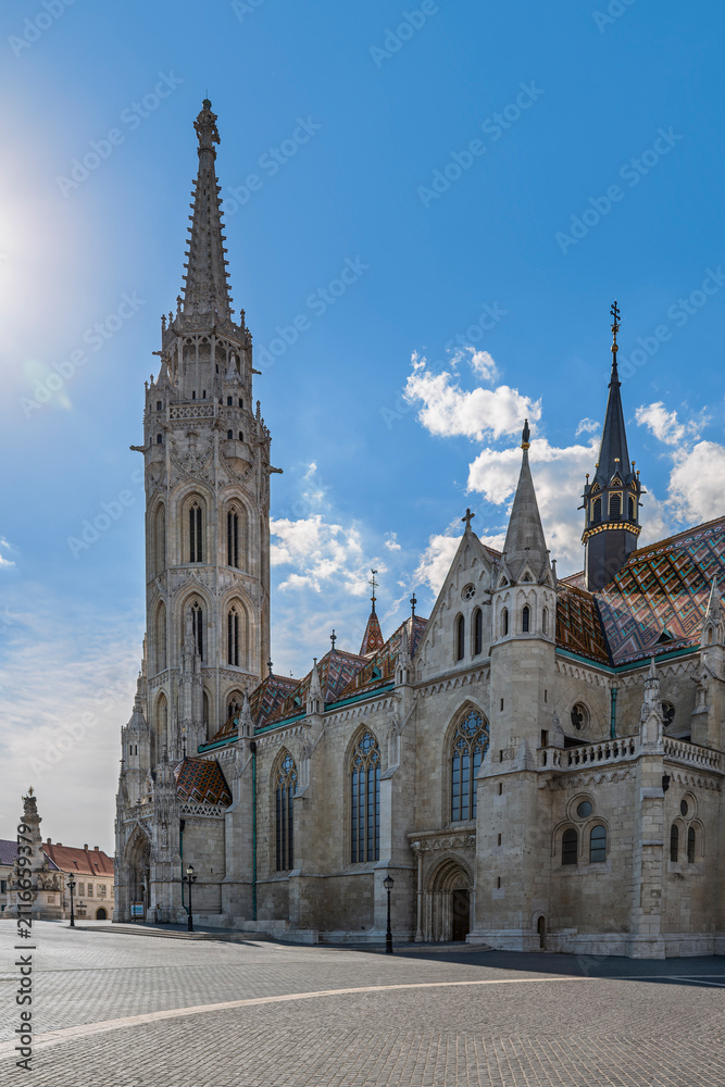 Fototapeta premium Full view of Matthias Church with its Gothic tower and colorful roof overlooking an empty square in Budapest, Hungary