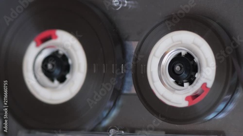 Extreme close up of a retro audio cassette tape spools spinning inside a transparent player. Vintage analog magnetic tape playing music from the 80s and 90s era