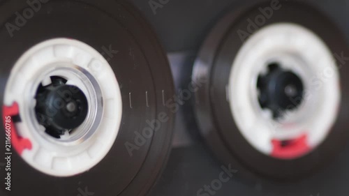 Extreme close up of a retro audio cassette tape spools spinning inside a transparent player. Vintage analog magnetic tape playing music from the 80s and 90s era.