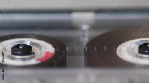Macro extreme close up of audio cassette tape spinning inside player during music playback. Vintage analogue media technology creates nostalgic feeling of classic sound format.