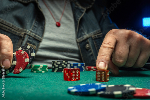 Fotografie A man rolls dice and stacks poker chips on a green table