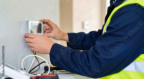 Electrician installing smart home thermostat. Professional technician mounting digital control device on wall. Smart home automation concept