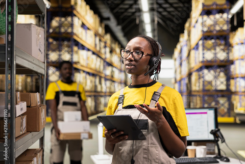 Принти на полотні A female warehouse worker answers client calls on a headset in a depot, handling problems and delays via a customer service helpline; a call center clerk troubleshoots shipment issues