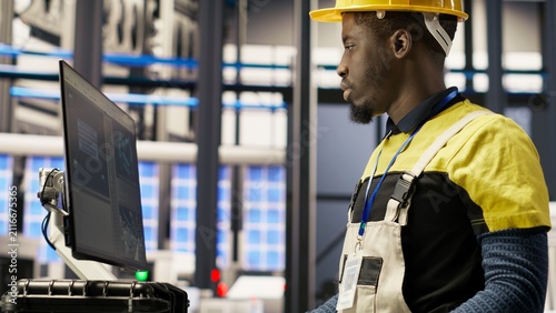 Bild auf Leinwand Solar plant engineer uses a computer to oversee systems, keeping machinery efficient; photovoltaic plant worker uses computer software to maintain continuous operations, along the production line