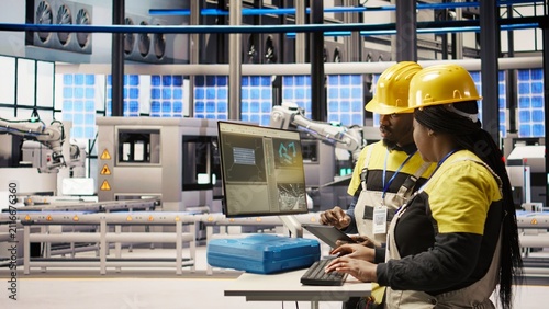 Фотография An engineering team uses a PC to oversee robotic assembly lines and manufacturing quality; collaborating colleagues monitor automated conveyor belts and factory operations during production